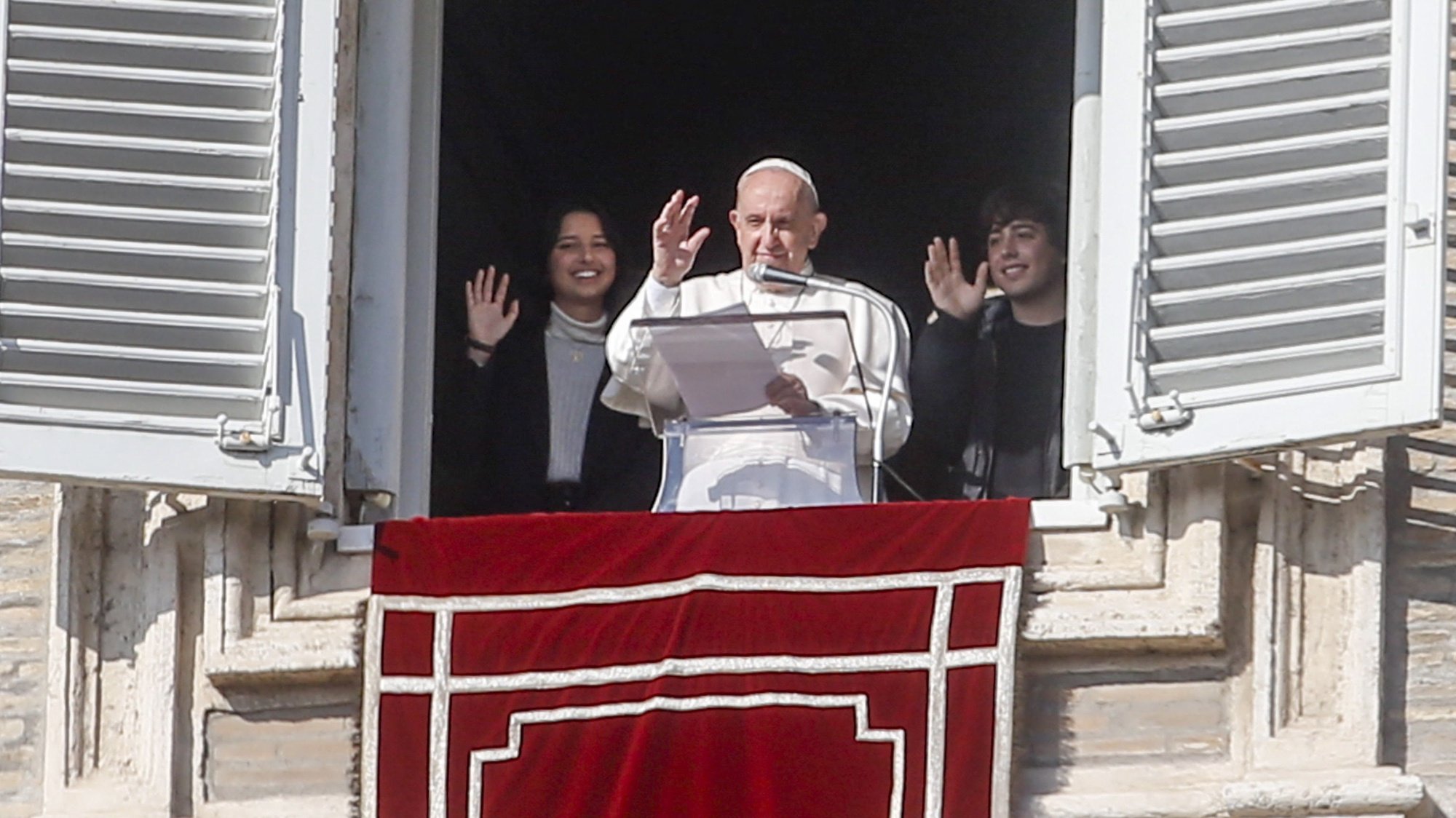 epa09595295 Pope Francis, flanked by two young people, waves from the window of his office overlooking Saint Peter&#039;s Square as he leads the recitation of the Angelus prayer, in Vatican City, 21 November 2021.  EPA/FABIO FRUSTACI