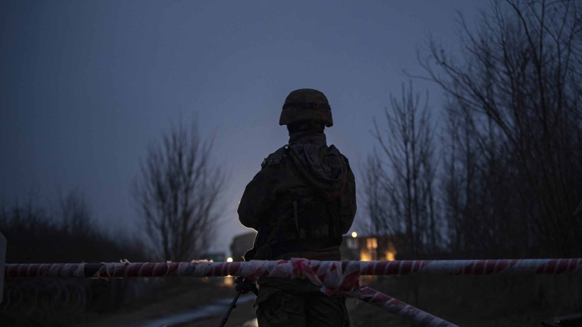 epa09623600 A soldier stands guard at the entrance to a temporary base outside the city of Michalowo, near the Polish-Belarusian border, eastern Poland, 16 November 2021. Poland has been struggling to stem the flow of asylum-seekers, refugees and migrants crossing into the country from Belarus. The Polish government said the migrants have been invited to Belarus by the Belarusian president, allegedly under the promise they will be able to live in the EU. Thousands of people who want to obtain asylum in the European Union have been trapped at low temperatures at the border since 08 November.  EPA/MARTIN DIVISEK