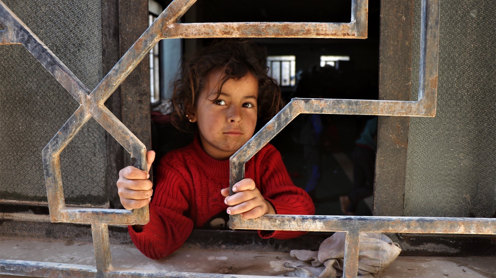 epa09708901 A displaced Syrian little girl looks through a window as she waits with her family at a mosque in Hasaka town, northeastern of Syria, 25 January 2022. According to the United Nations, around 45,000 people fled their homes in Hasaka city, due to the ongoing clashes between the Fighters of the Syrian democratic forces (SDF) and fighters of the Islamic State, following IS fighters attacking Ghweran and al-Shaddadi prisons in al-Hasaka on 20 January 2022, to break thousands of its affiliates out of the prison.  EPA/AHMED MARDNLI