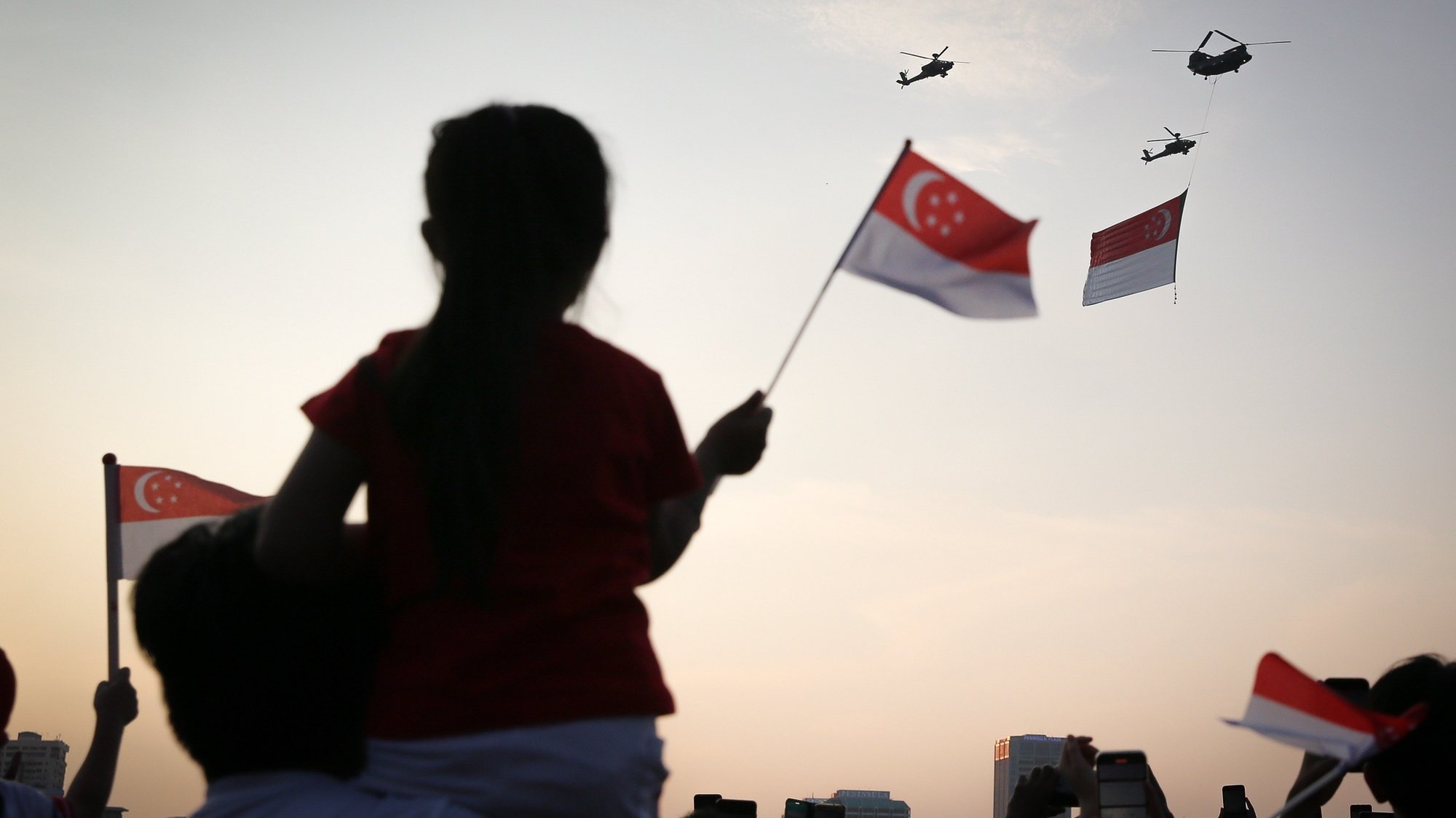 epa10112768 Spectators wave flags as helicopters fly past with the national flag during the National Day Parade in Singapore, 09 August 2022. Singapore celebrates its 57th birthday on 09 August 2022 with its first full parade since the coronavirus disease (COVID-19) pandemic.  EPA/ONG WEE JIN/THE STRAITS TIMES SINGAPORE OUT  EDITORIAL USE ONLY