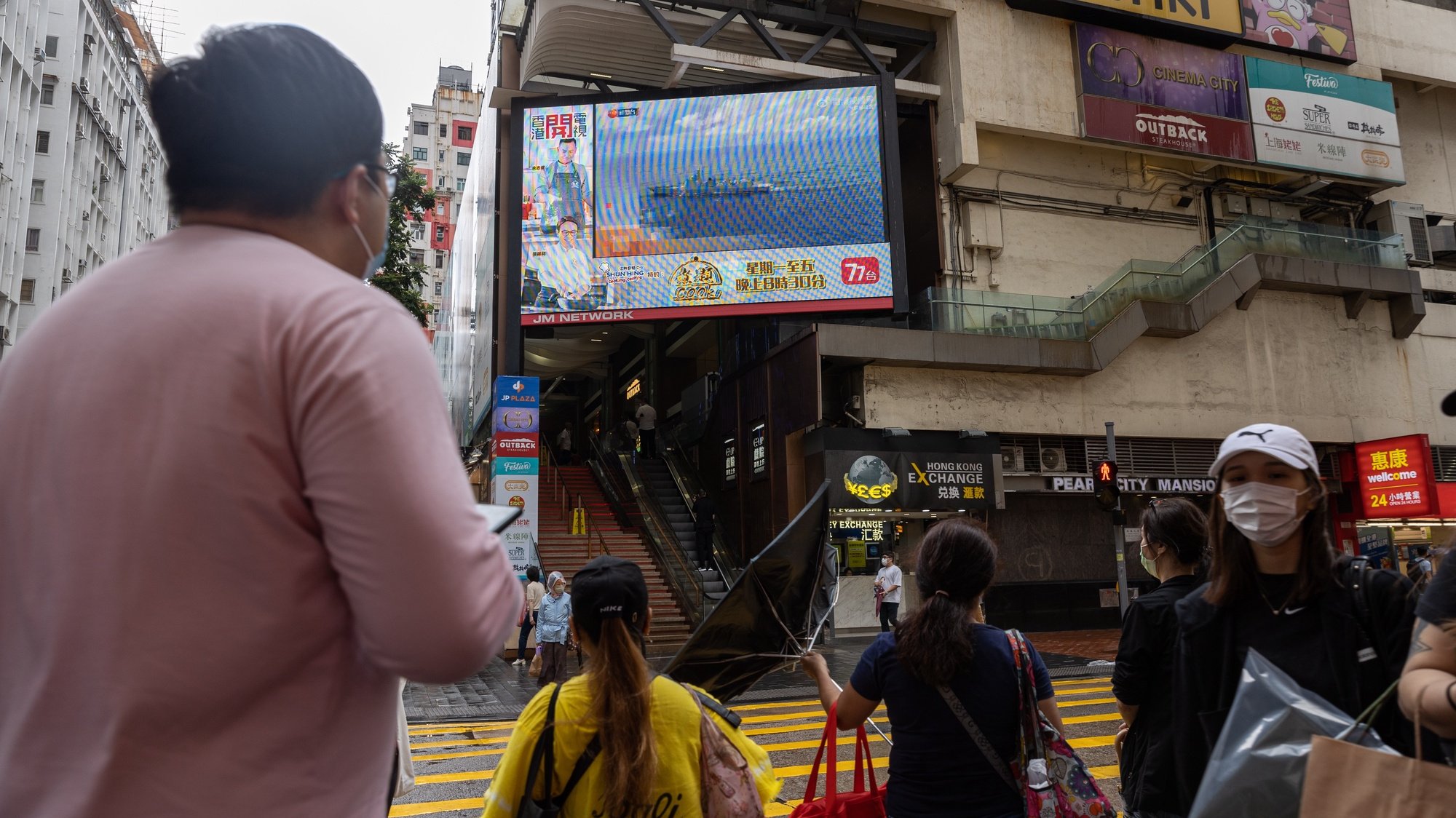 epa10112252 Pedestrians walk at a street past a large TV-screen displaying news broadcasting of a China&#039;s People&#039;s Liberation Army (PLA) warship, in Hong Kong, China, 09 August 2022. Beijing has announced its navy and air force would continue joint live-fire drills in the waters and airspace around Taiwan.  EPA/JEROME FAVRE
