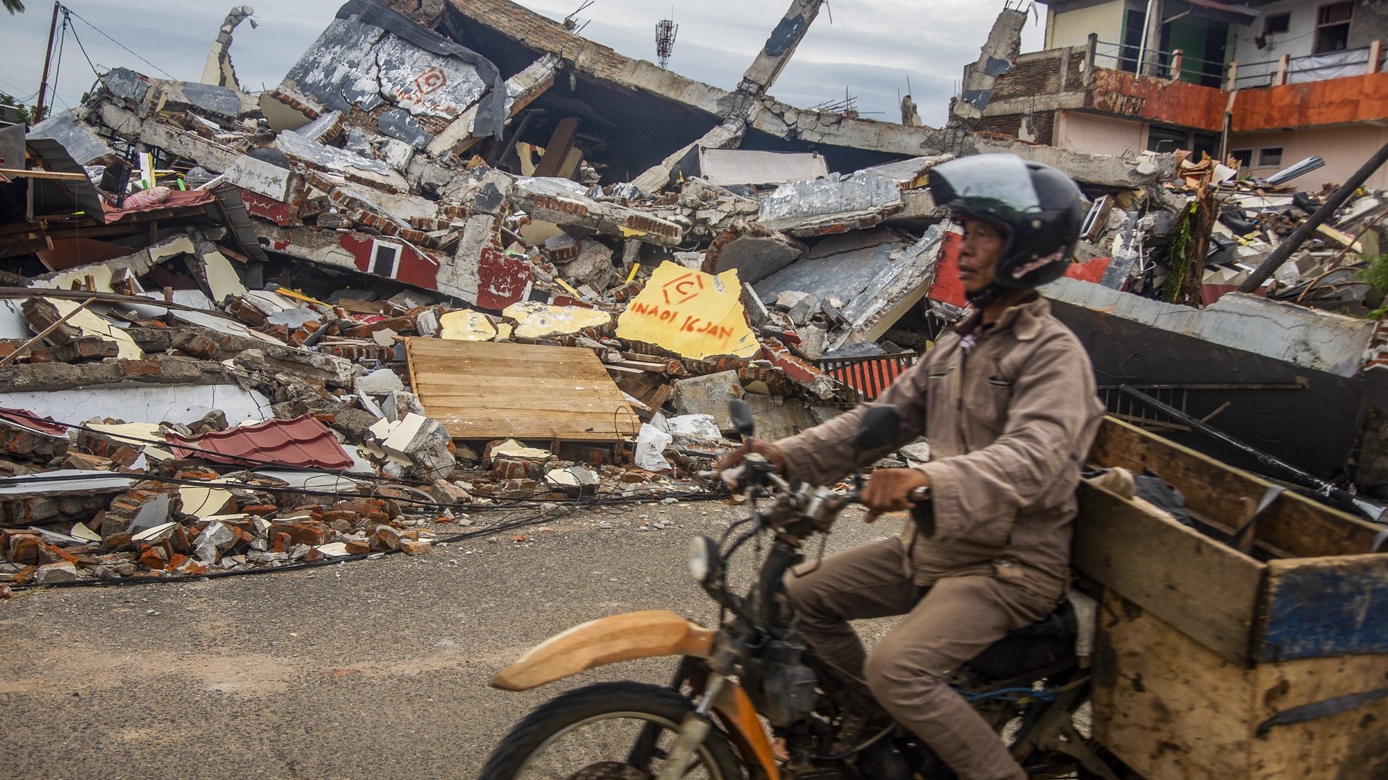 epa08942953 A man rides his motorbike past collapsed houses in the aftermath of an earthquake in Mamuju, West Sulawesi, Indonesia, 17 January 2021. At least 56 people were killed and hundreds injured after a 6.2 magnitude earthquake struck Sulawesi island on 15 January.  EPA/IQBAL LUBIS