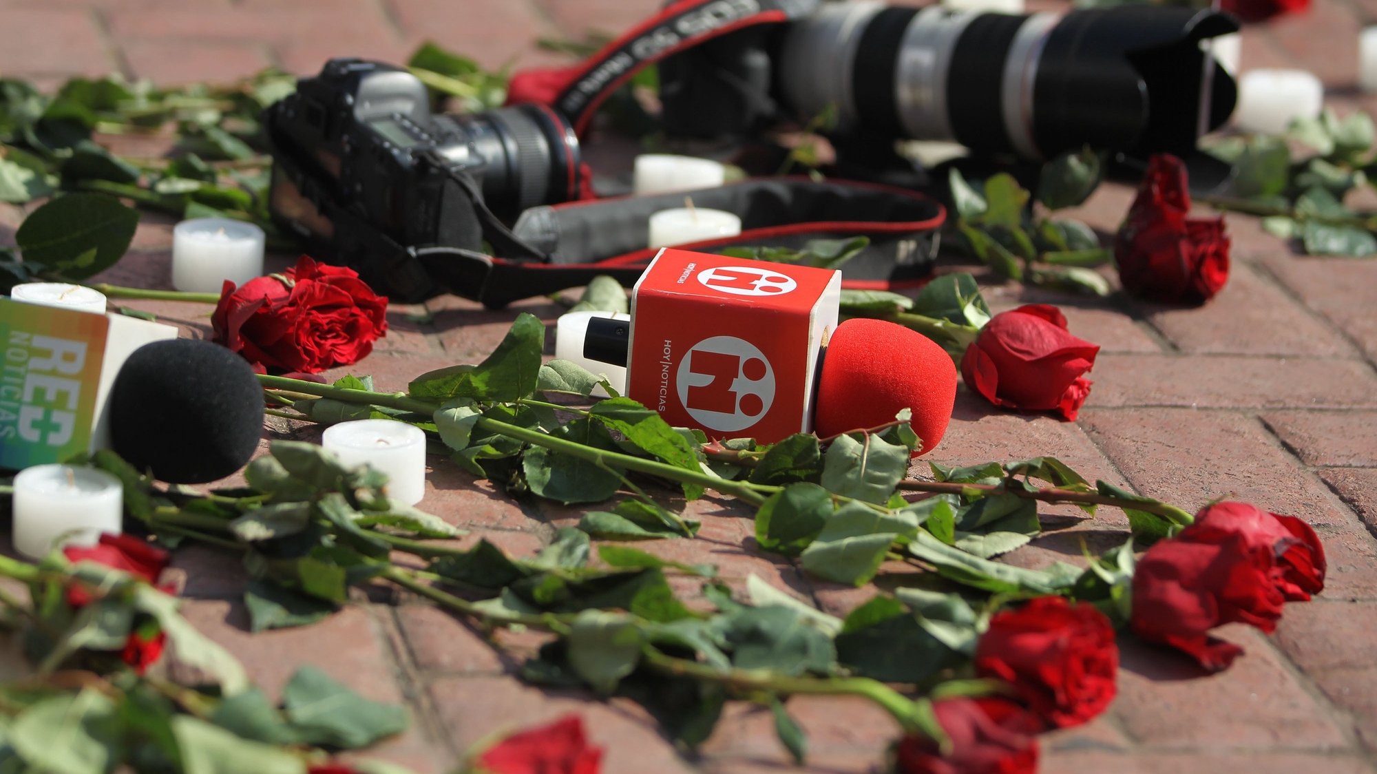 Câmaras e microfones no chão perto de um ramo de rosas para prestar homenagem aos jornalistas assassinados no México