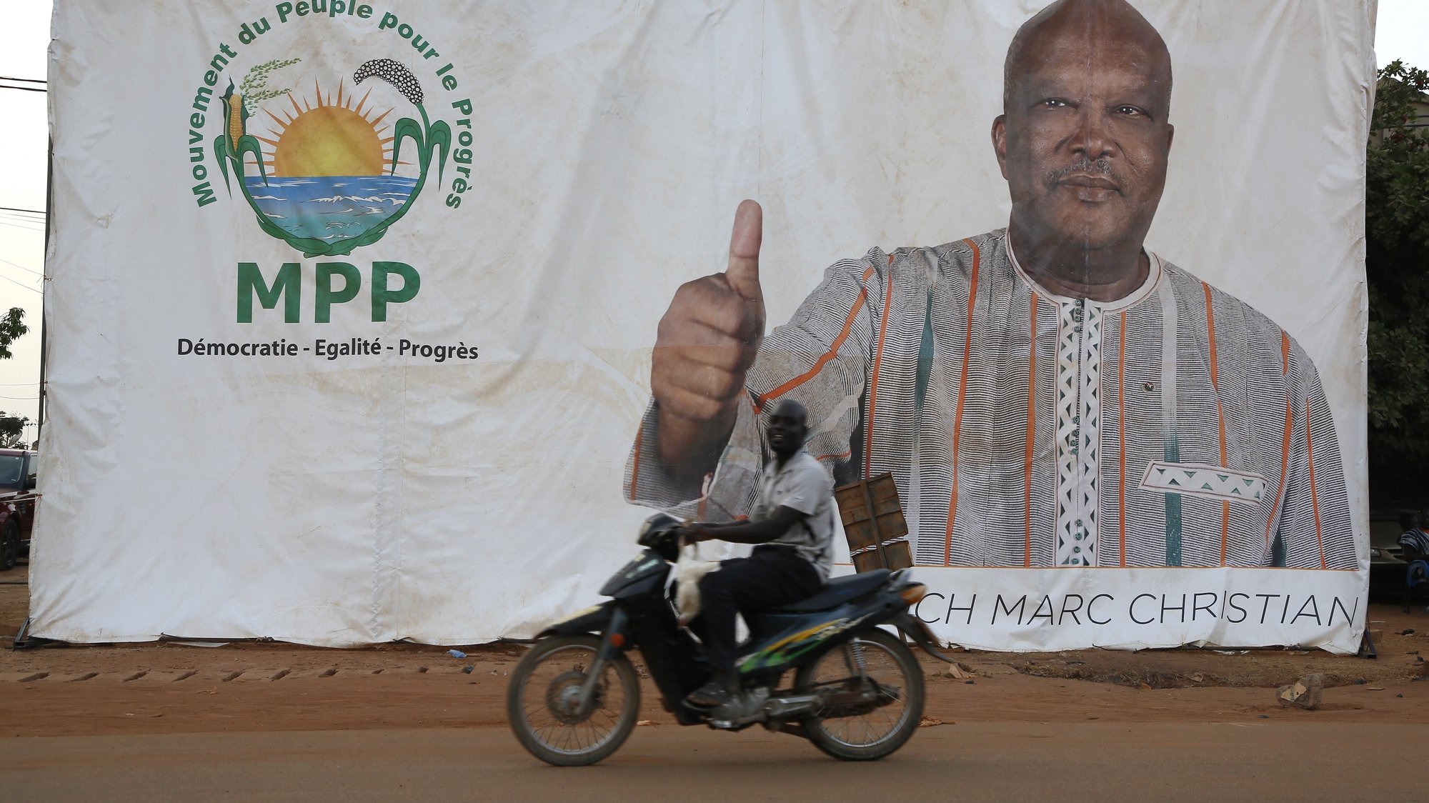 epa08829737 A man rides on a motorcycle past an election poster by outgoing President Roch Marc Christian Kabore, in Ouagadougou, Burkina Faso, 19 November 2020. The first round of the presidential election in Burkina Faso will take place on 22 November  2020.  EPA/LEGNAN KOULA