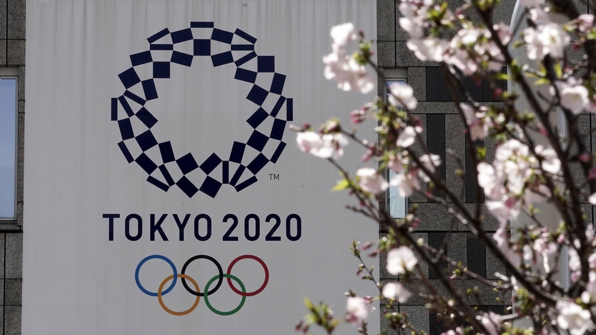 epa08338045 The logo of the Tokyo 2020 Olympic Games hangs from a wall behind cherry blossoms in Tokyo, Japan, 02 April 2020. Tokyo Governor Yuriko Koike warned the city is going through an important phase in preventing further spread of COVID-19. The Tokyo 2020 Olympics organizing committee and the International Olympic Committee (IOC) announced on 30 March 2020 that the Games would be rescheduled to 23 July 2021 amid the ongoing coronavirus pandemic that forced the event’s one year postponement.  EPA/KIMIMASA MAYAMA