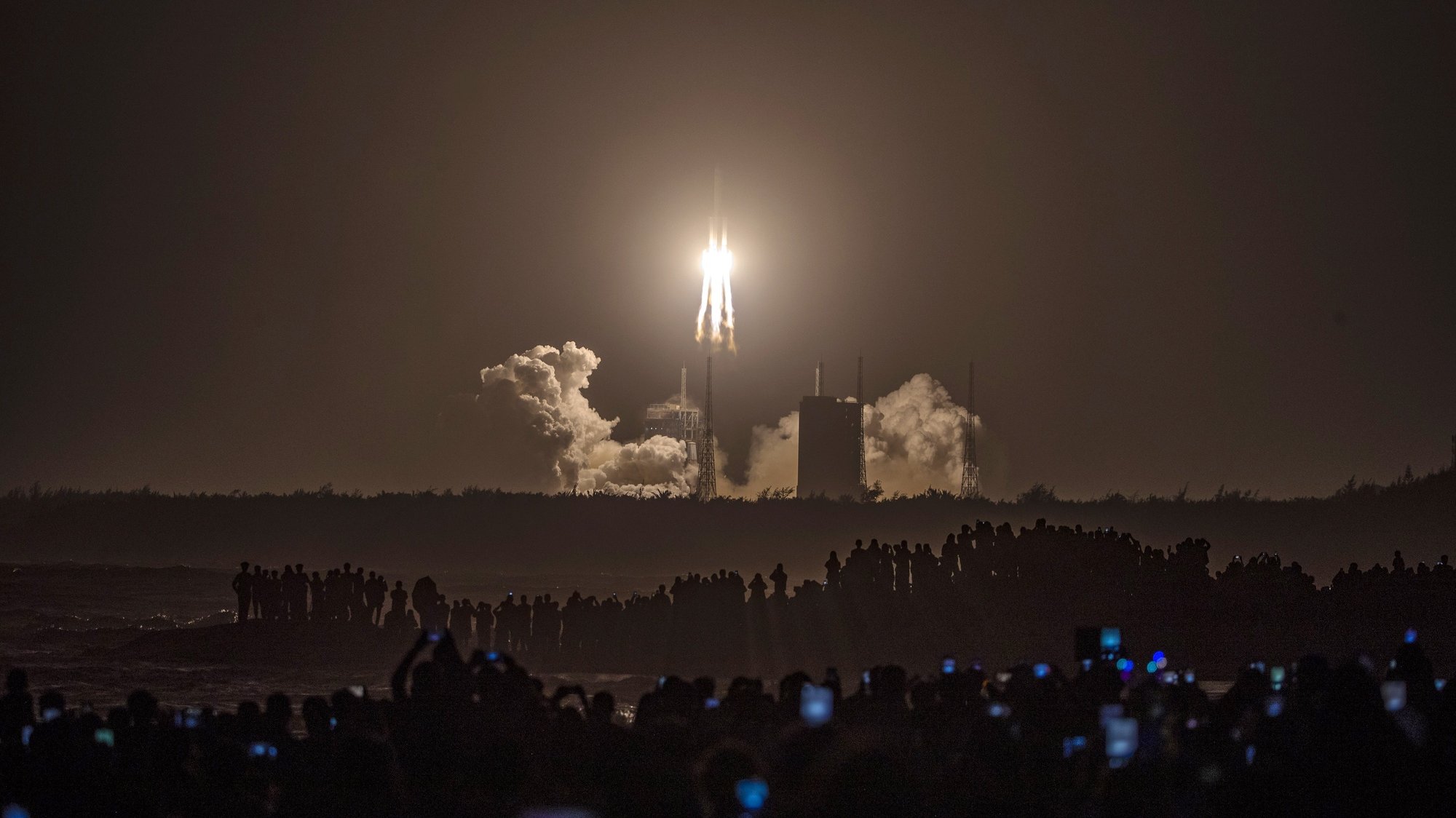 epa08838329 People watch a Long March 5 rocket carrying the Chang&#039;e-5 lunar probe launching from the Wenchang Space Center in Wenchang, Hainan Island, China, 24 November 2020. China launched a mission to the Moon with an unmanned spacecraft on 24 November 2020 to bring back lunar rocks, the first country to attempt to retrieve material from the Moon in decades.  EPA/STR CHINA OUT