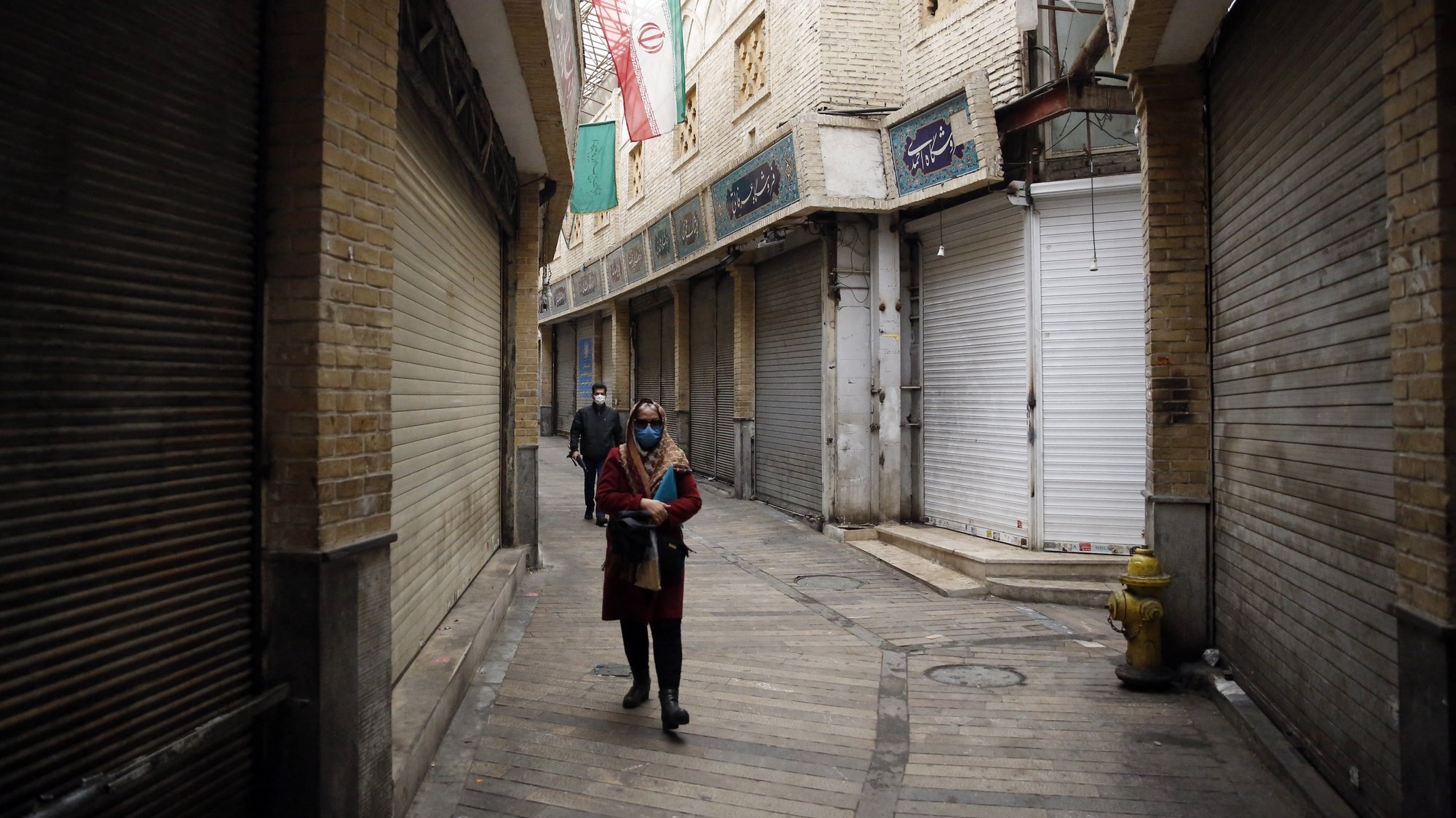 epa08837147 Iranians wearing face masks walk next to closed shops in Tajrish old bazaar  in Tehran, Iran, 23 November 2020. Iranian authorities began a two-week lockdown from 21 November to slow the spread of the Covid-19 in Iran.  EPA/ABEDIN TAHERKENAREH