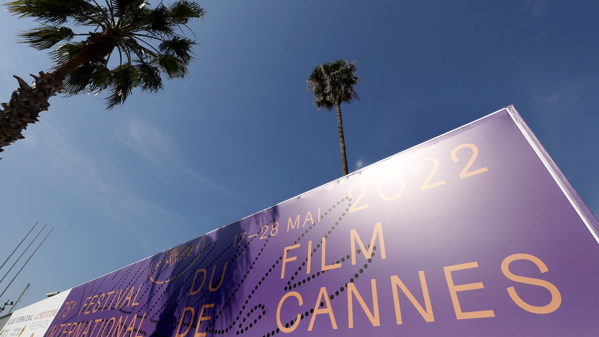 epa09948284 A view of a palm tree behind a giant canvas of the official poster of the 75th annual Cannes Film Festival on the Palais des Festivals facade in Cannes, France, 15 May 2022. The festival runs from 17 to 28 May.  EPA/SEBASTIEN NOGIER