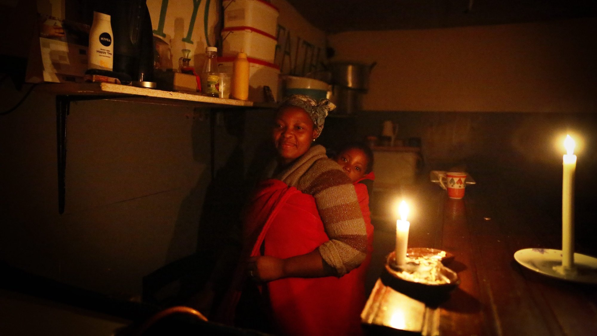 epa04769428 A South African woman carrying her daughter on her back runs her take away restaurant by candle light during a sheduled power outage known as load shedding in the impoverished neighbourhood of Masiphumelele, Cape Town, South Africa 26 May 2015. Large scale industries as well as small businesses are feeling the pinch of South Africa&#039;s beleaguered state run power utility, Eskom. Eskoms inability to meet electricity demand has resulted in a tortuous schedule of rolling blackouts known as Load Shedding which is having a negative effect on the economy. Load Shedding is expected to last several years until the poorly maintained power plants can return to full capacity and the new power plants are completed before proper service can resume to the country.  EPA/NIC BOTHMA