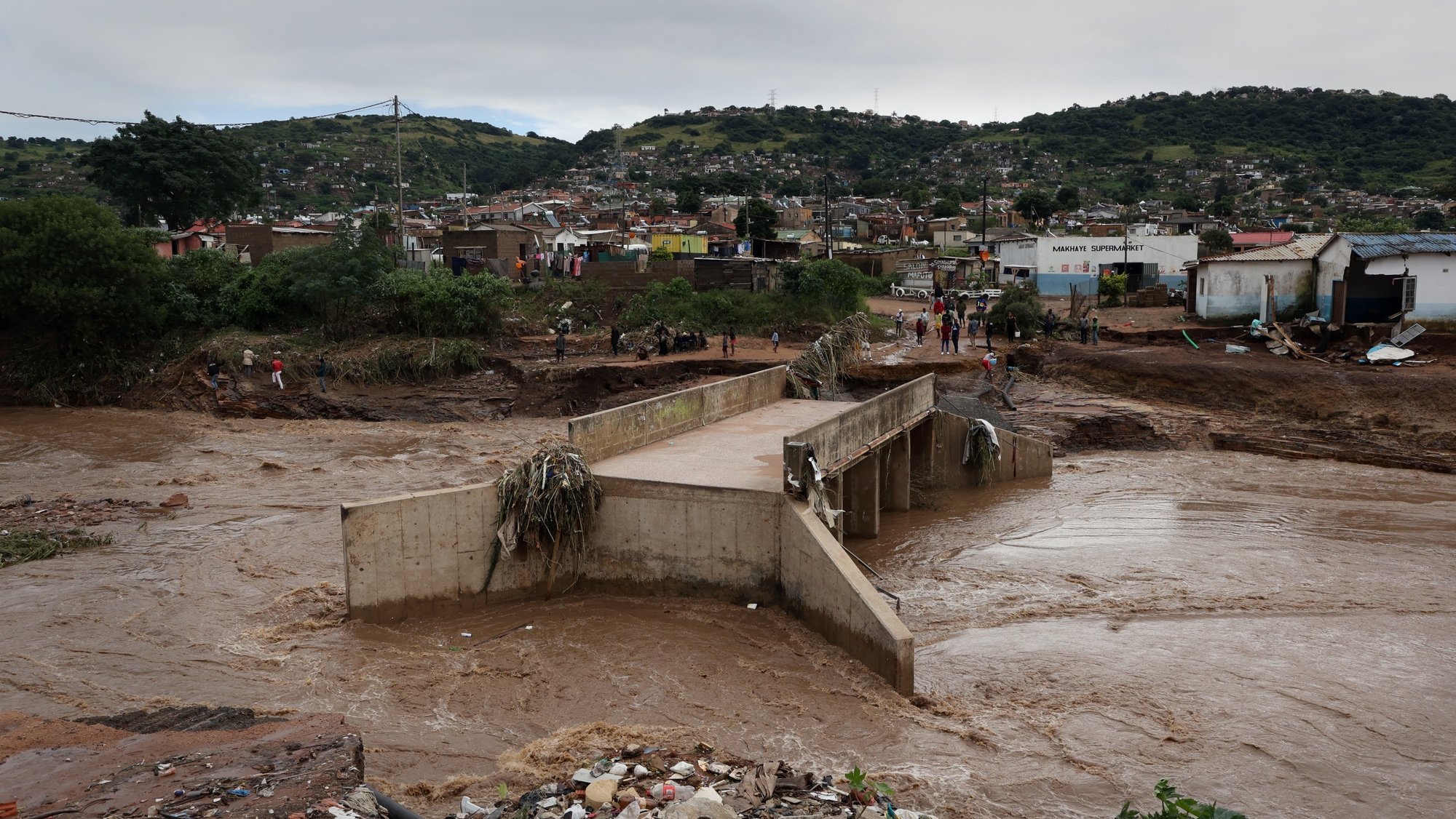 epa09886250 A river runs around a damaged bridge after heavy rains destroyed it near Durban, South Africa, 12 April 2022. At least 45 people have died as a result of heavy flooding in the Eastern Coastal area. Key roads in the area have been damaged and as mudslides destroyed houses. The South African National Defense Force have been called in to assist.  EPA/STR