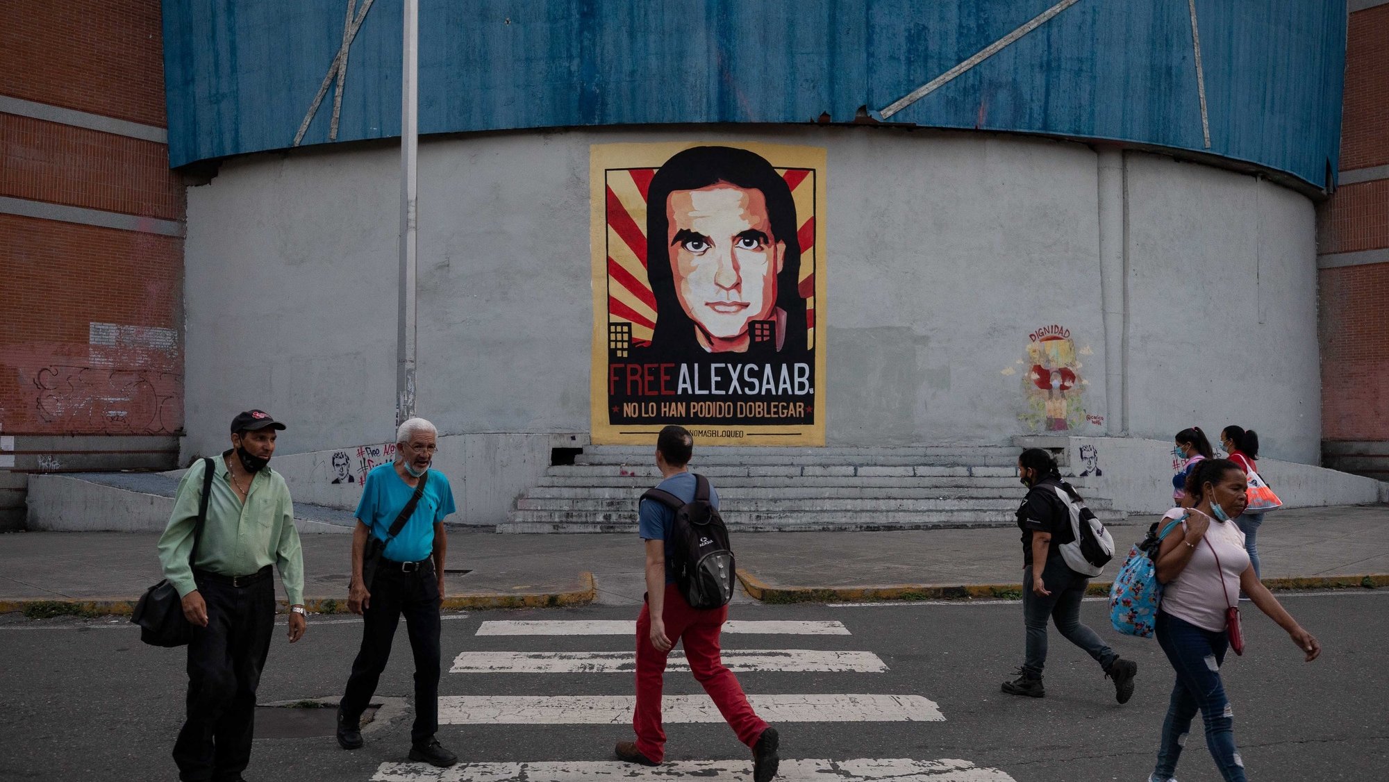 epa09547066 People walk in front of a mural with the image of Alex Saab, alleged front man of the President of Venezuela, Nicolas Maduro, in Caracas, Venezuela, 25 October 2021.  EPA/Rayner Pena R.