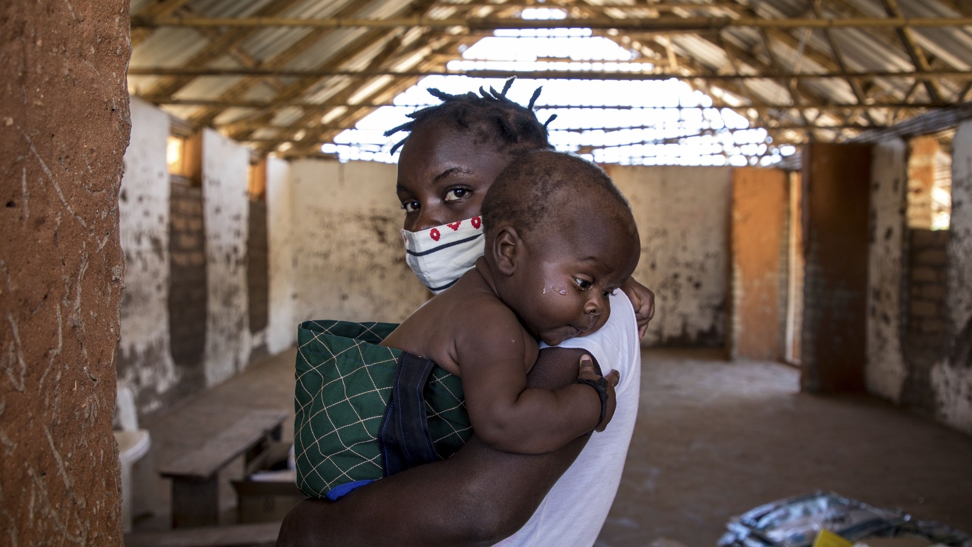 Mãe e filho aguardam pela consulta de uma brigada móvel do Fundo das Nações Unidas para a Infância (UNICEF), um grupo de profissionais de saúde que viaja de ambulância e vai ao encontro das comunidades mais afastadas em vez de esperar por elas em centros de saúde, Impire, Moçambique, 24 de julho de 2020. Em menos de uma hora, na povoação de Impire, distrito de Metuge, sul de Cabo Delgado, juntam-se dezenas de mães com as suas crianças - a maioria ainda bebés - para a brigada observar, com pesagem, medição de altura, avaliação à subnutrição, seguindo-se uma consulta, vacinação e entrega da medicamentos numa rotina que inclui a observação das mães e decorre desde manhã até o sol se pôr, num pavilhão empoeirado. (ACOMPANHA TEXTO DE 25 DE JULHO DE 2020). RICARDO FRANCO/LUSA