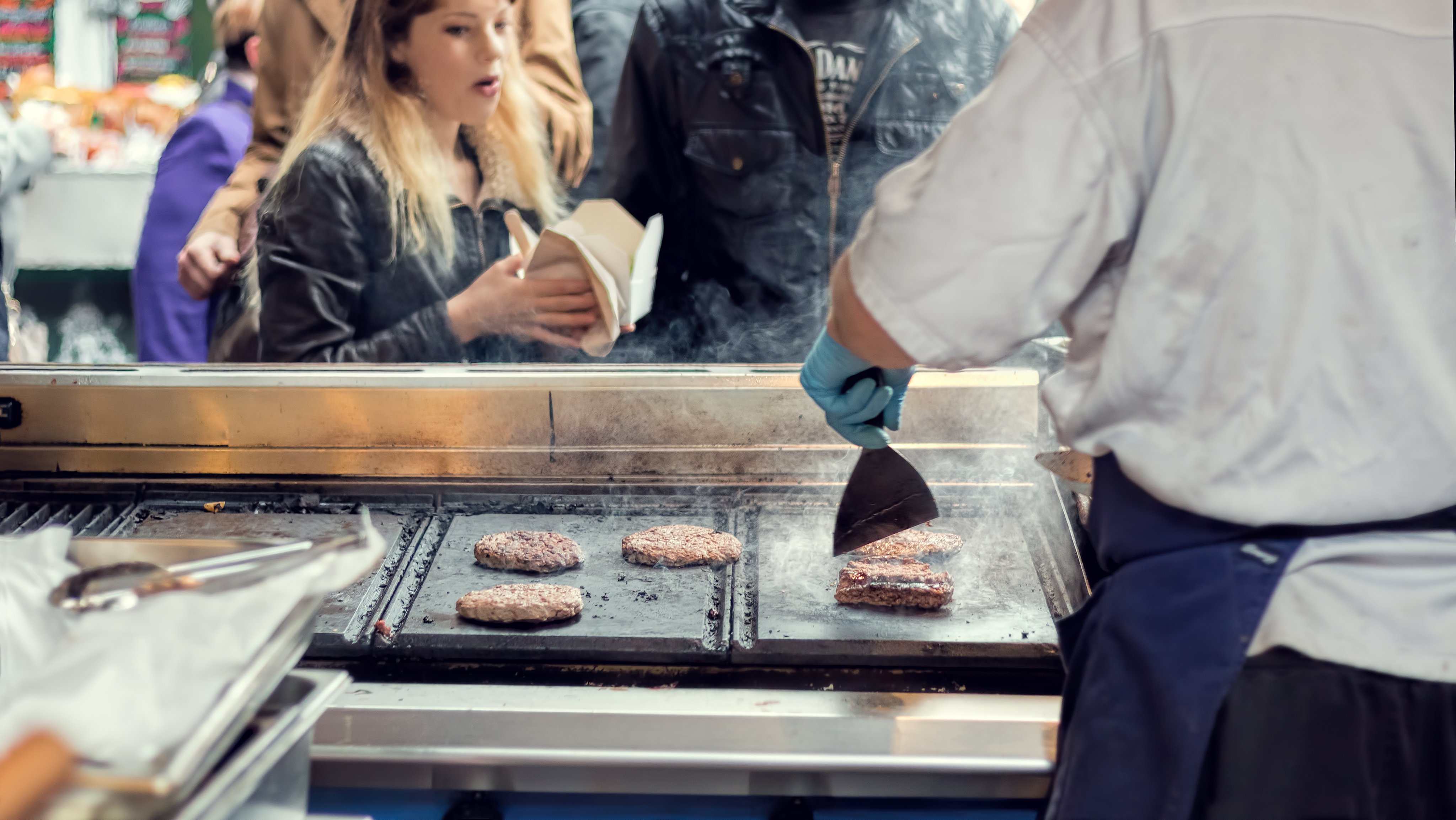 Street food vendor grills burgers for customers.
