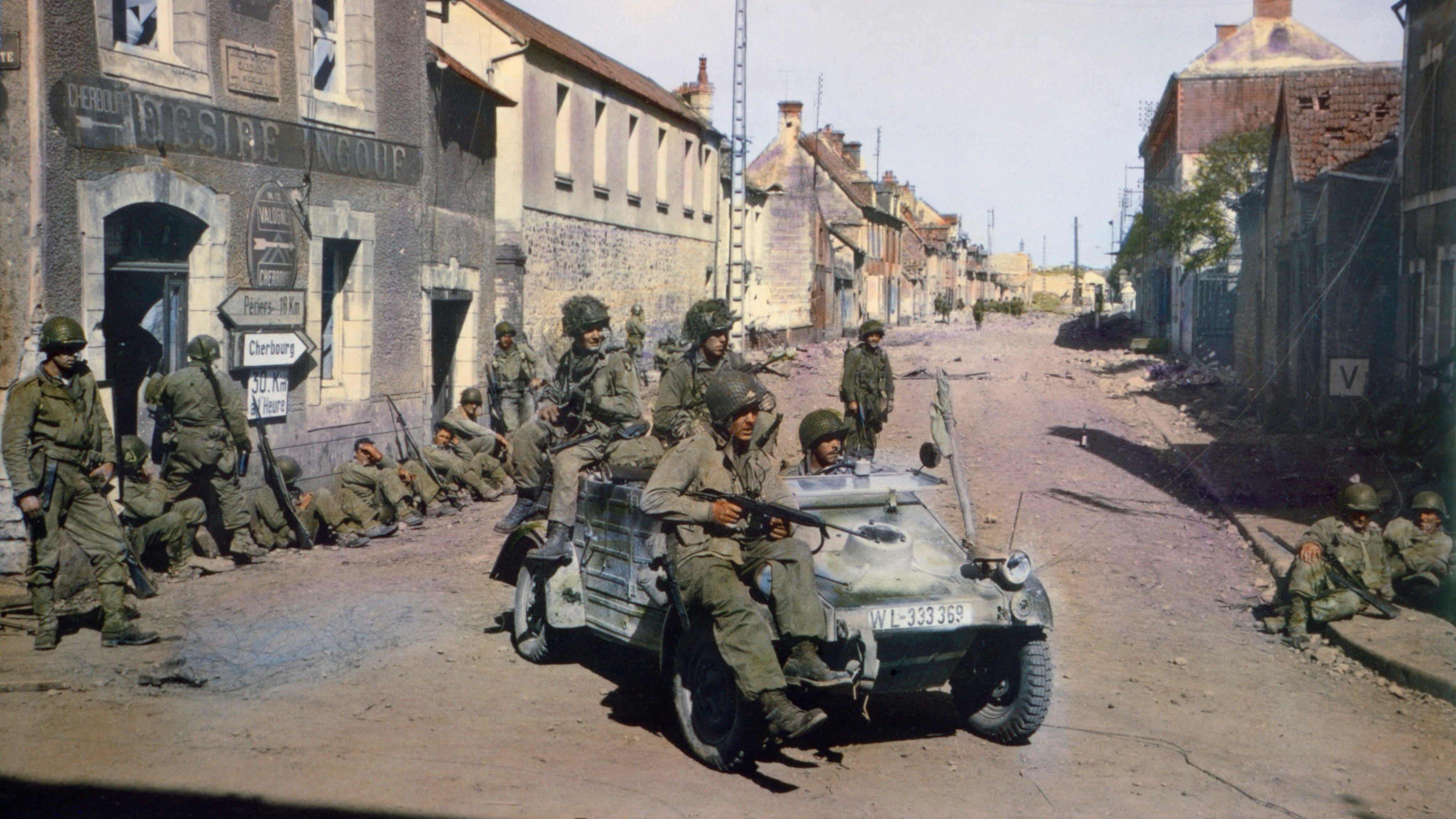 American Paratroopers in Captured German Jeep Patrolling Carentan while other American Soldiers Rest against a Building, Normandy