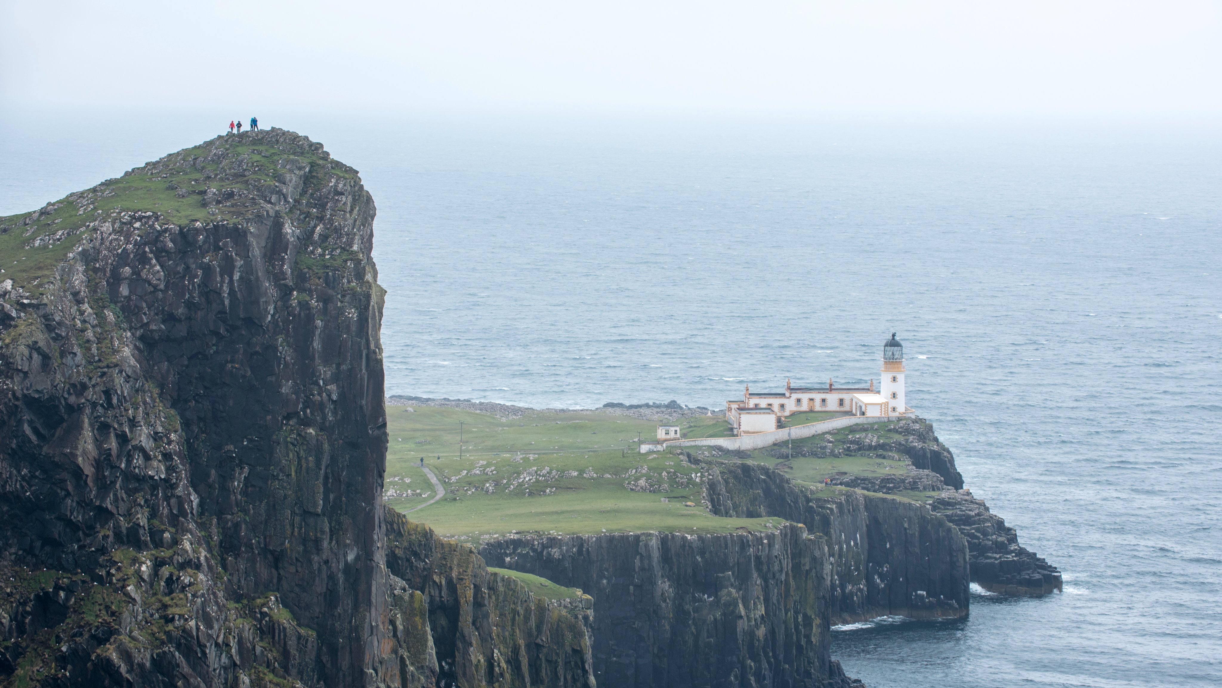 Walkers on clifftop watching Neist Point Lighthouse.