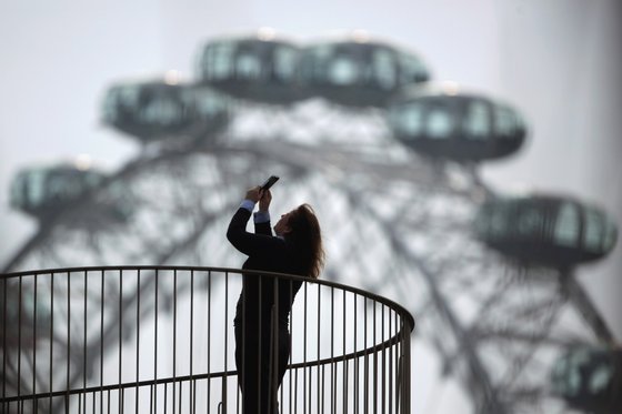LONDON, ENGLAND - MARCH 22: A woman takes a photograph from a balcony near the London Eye on March 22, 2012 in London, England. A full rotation of the giant Ferris wheel, the largest of it's kind in Europe, takes 30 minutes and rises to a height of 135 metres. On a clear day one can see for 40km from the top. (Photo by Dan Kitwood/Getty Images)
