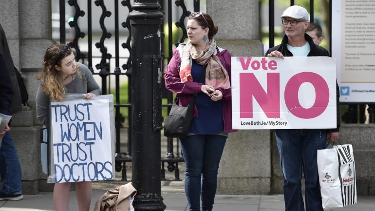 Uma apoiante do &quot;Sim&quot; olha para um cartaz de um defensor do &quot;Não&quot;, em Dublin