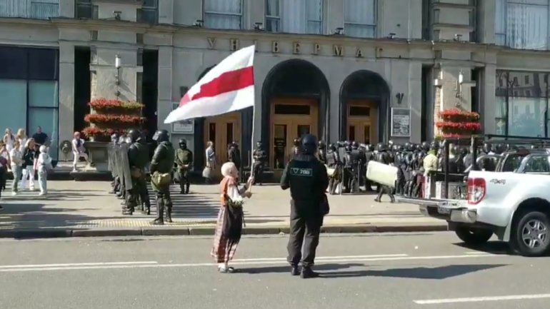 Nina Bahinskaya à frente de um polícia a empunhar a bandeira da antiga República Popular da Bielorrússia